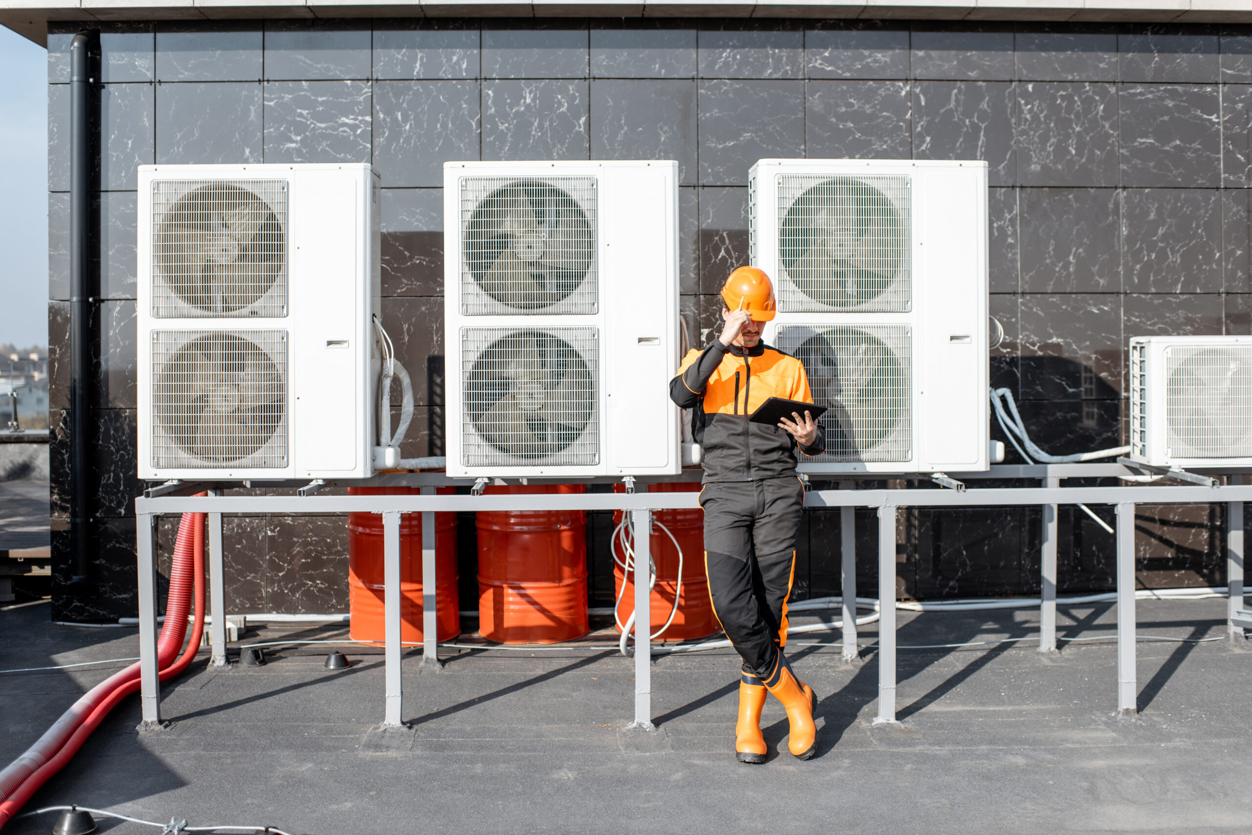 Technician in safety gear using digital tablet to inspect rooftop HVAC system as part of proactive maintenance program